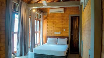 Un dormitorio con cama, ventana con cortinas, pared de ladrillo y aire acondicionado.