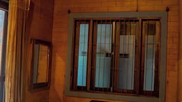 Una habitación con cama, ventana con barrotes, ventilador de techo y unidad de aire acondicionado.
