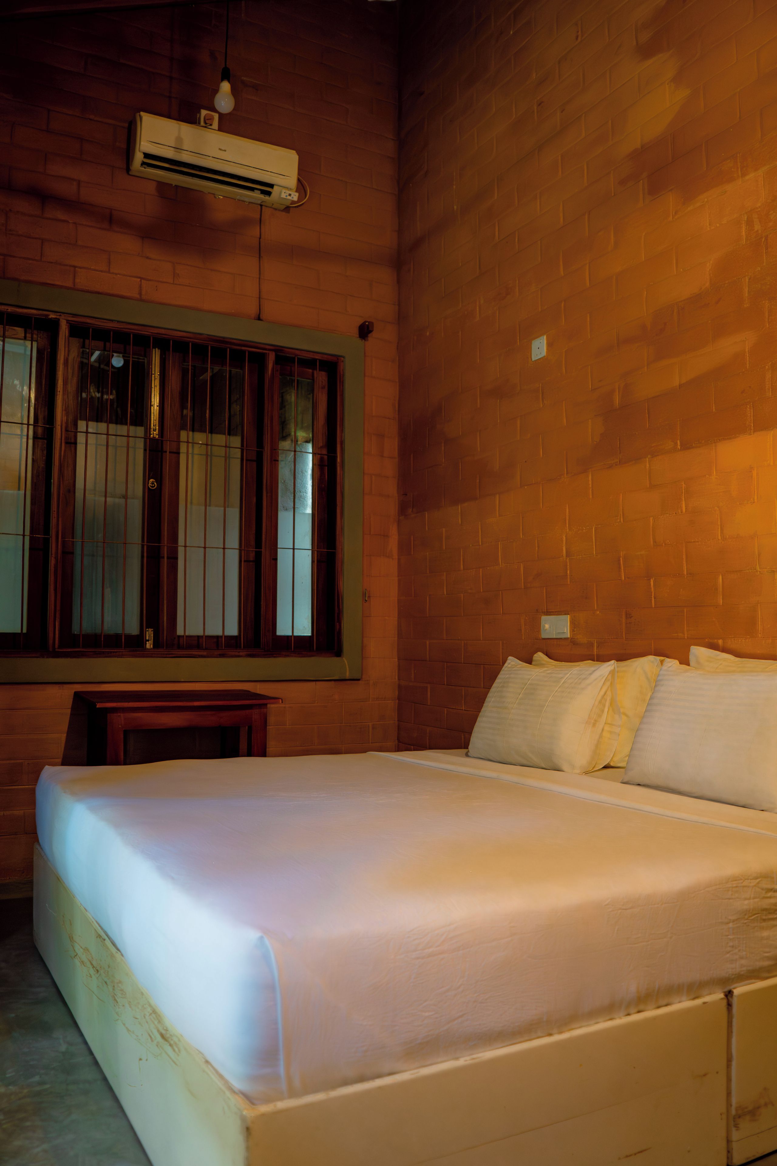 A room with a bed, a window with bars, and a brick wall.