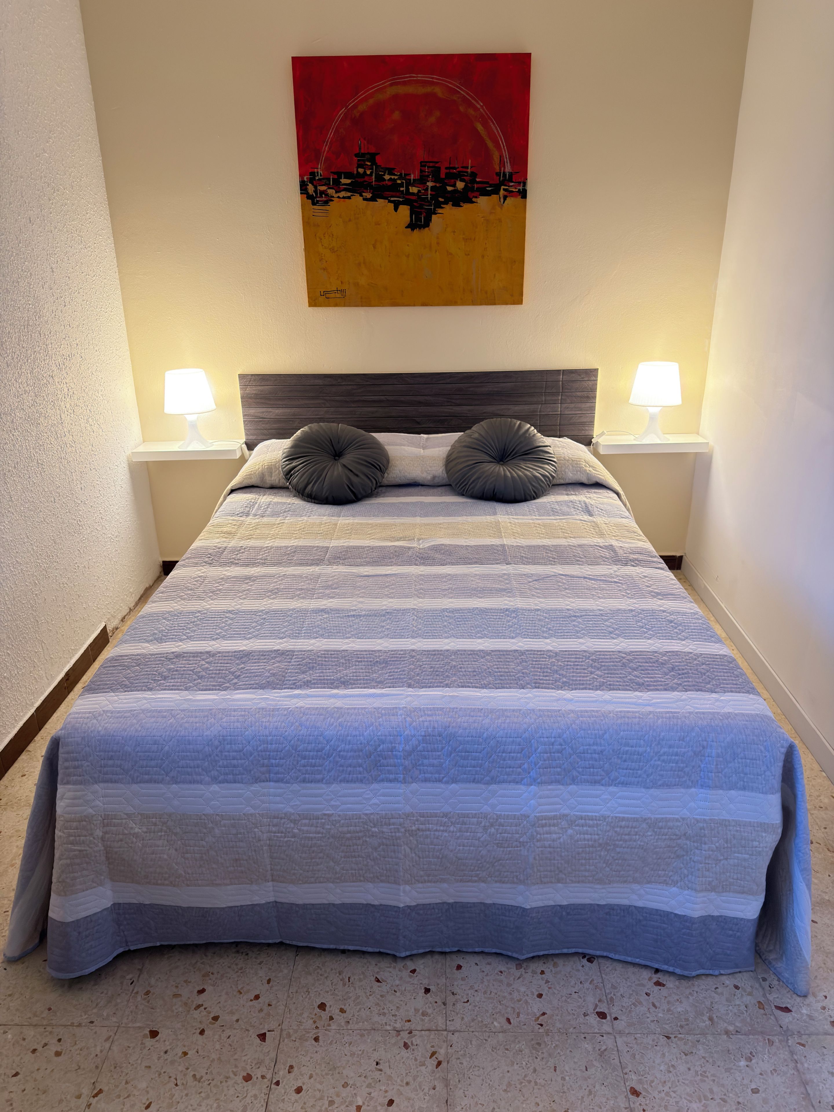 A neatly made bed with a striped bedspread, two bedside lamps, and a wall-mounted artwork.