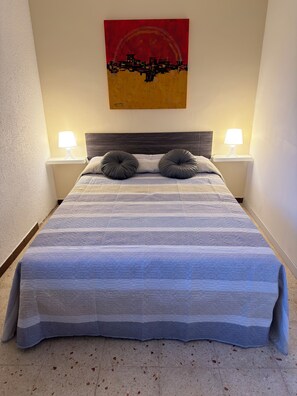 Een net opgemaakt bed met een gestreept dekbedovertrek, twee bedlampen en een kunstwerk aan de muur.