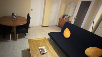 Een woonkamer met een donkere bank, een houten salontafel, een eettafel met stoelen en een klein decoratief object op tafel.