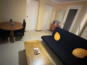 Een woonkamer met een donkere bank, een houten salontafel, een eettafel met stoelen en een klein decoratief object op tafel.