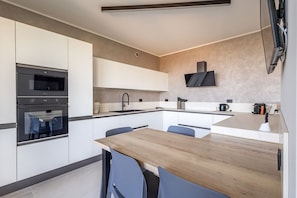 A modern kitchen with a wooden dining table, built-in appliances, and a flat-screen TV mounted on the wall.