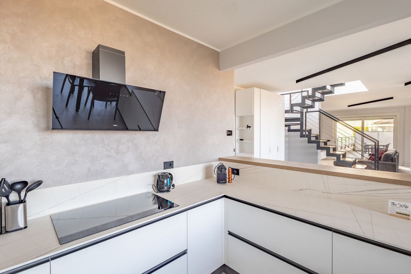 A modern kitchen with a large flat-screen TV, a marble countertop, and a staircase leading to a balcony.