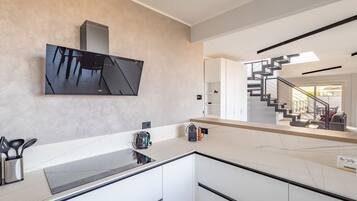 A modern kitchen with a large flat-screen TV, a marble countertop, and a staircase leading to a balcony.