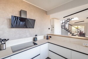 Una cocina moderna con una amplia pantalla plana, encimera de mármol y una escalera que lleva a un balcón.