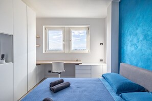 A bedroom with a bed, a desk, and a window.