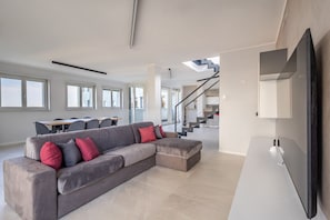 A spacious living area with a sectional sofa, a dining table, and a staircase leading to an upper floor.