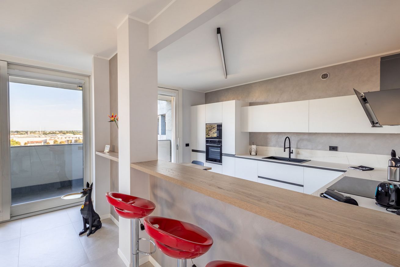 Una cocina moderna con un ventanal grande, un perro y taburetes rojos.