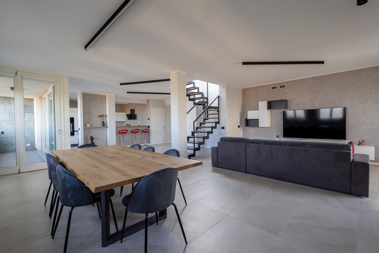 A modern living space with a dining area, a sofa, a TV, and a staircase.