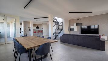A modern living space with a dining area, a sofa, a TV, and a staircase.