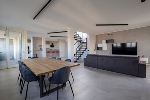 Un espacio habitable moderno con comedor, sofá, televisor y escalera.