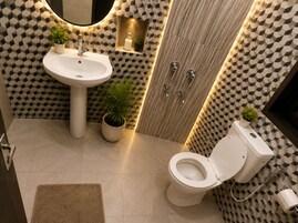 Un baño con lavamanos blanco, inodoro y zona de ducha. Hay plantas y un espejo en la pared.