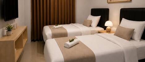 A hotel room with two beds, a flat-screen TV, a bedside table with a lamp, and a painting on the wall.
