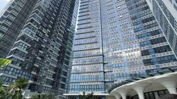 A modern high-rise building with a glass facade, a pool area with a white structure, and a well-maintained lawn.