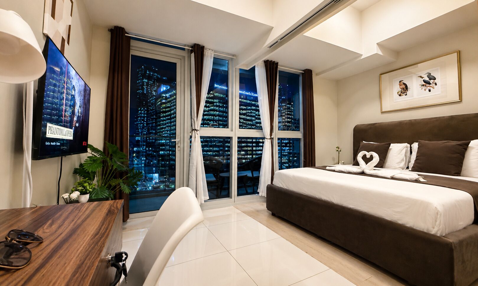 A hotel room with a bed, a desk, a chair, a TV, and a large window with a city view.