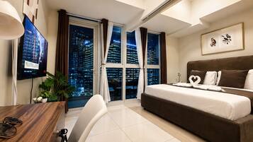 A hotel room with a bed, a desk, a chair, a TV, and a large window with a city view.