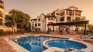 A swimming pool with lounge chairs and a pergola, surrounded by a fence and trees. - El Valle Golf Residence | Private Terraces & Pools (Murcia)