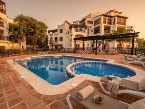 Ein Schwimmbecken mit Liegestühlen und einer Pergola, umgeben von einem Zaun und Bäumen.