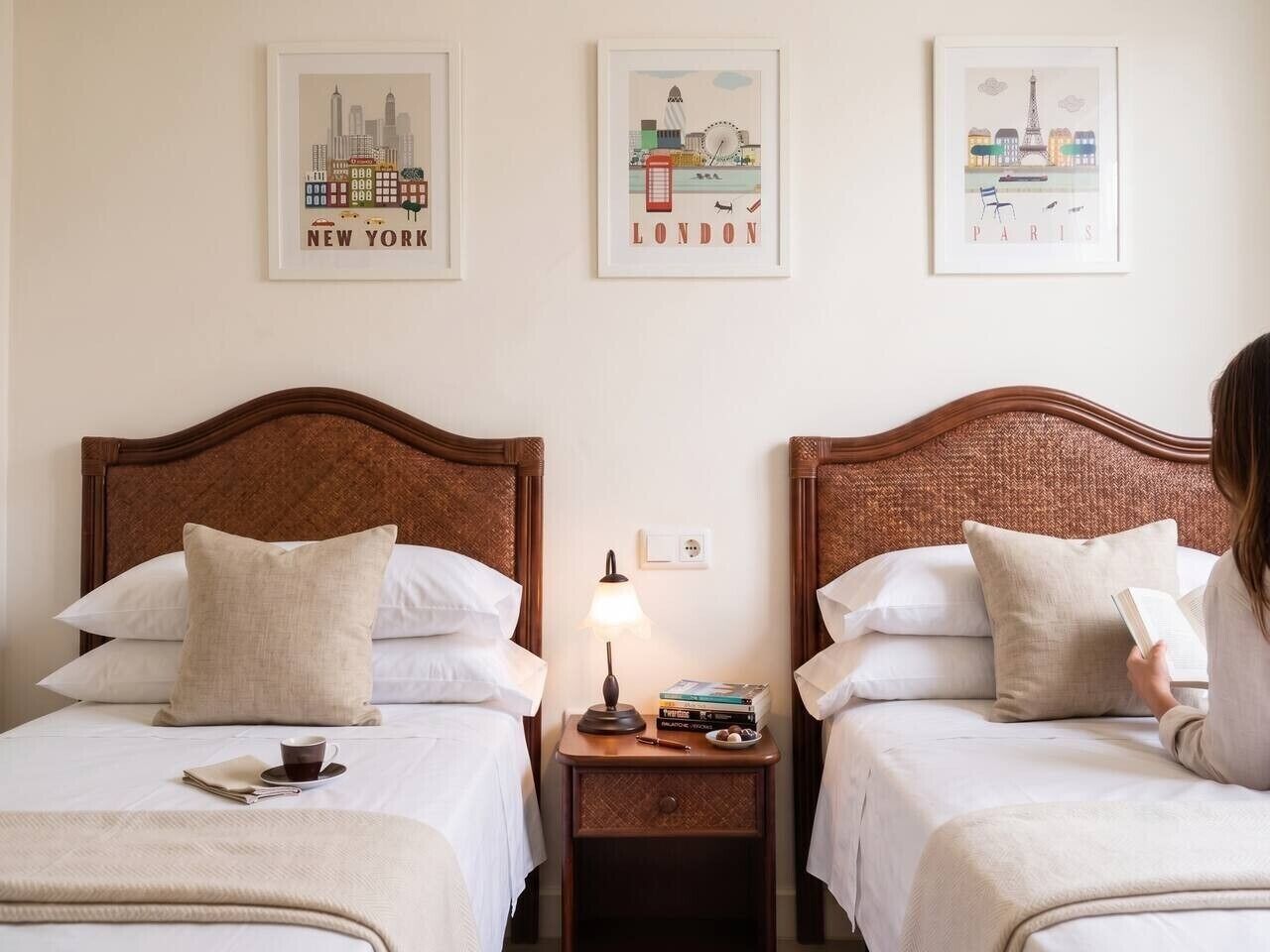 Une chambre d’hôtel avec deux lits, une table de chevet avec une lampe, un livre et une tasse.
