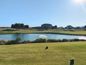 Un parcours de golf avec un étang, une colline au loin et un ciel dégagé.