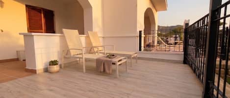 A balcony with a wooden floor, white furniture, and a railing.