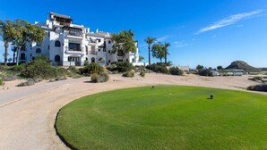 A golf course with a white building in the background, surrounded by greenery and palm trees. - El Valle Golf Residence | Private Terraces & Pools (Murcia)
