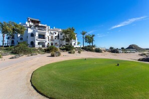 Ein Golfplatz mit einem weißen Gebäude im Hintergrund, umgeben von viel Grün und Palmen.