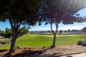 Ein Golfplatz mit Bäumen, blauem Himmel und Bergen in der Ferne.