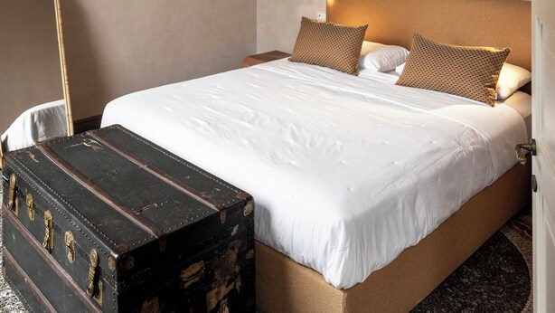 A hotel room with a large bed, a wooden headboard, a nightstand, a lamp, and a vintage suitcase. - Colombo Suites, the stunning Ligurian Riviera: a taste of nature and relaxation (Lavagna)