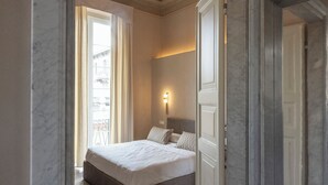 A hotel room with a bed, a nightstand, a wall-mounted light, and a view through a window. - Colombo Suites, the stunning Ligurian Riviera: a taste of nature and relaxation (Lavagna)
