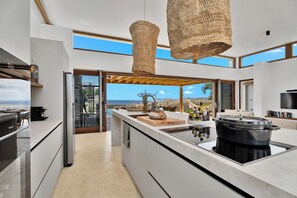 A modern kitchen with a large island, a view of the ocean, and a hanging woven light fixture. - Brand new luxury Bonaire villa with infinity pool, ocean views, and stunning sunsets. Kas Pajuro accommodates up to 10 guests and offers modern comfort in an exclusive location. (Kralendijk)