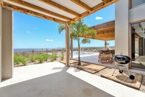 Un patio exterior con piscina, una parrilla y vistas al océano.