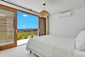Ein Schlafzimmer mit einem großen Bett, Blick ins Freie und einem Deckenventilator.