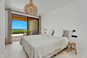 A bedroom with a bed, a nightstand, a lamp, and a view of the outdoors. - Brand new luxury Bonaire villa with infinity pool, ocean views, and stunning sunsets. Kas Pajuro accommodates up to 10 guests and offers modern comfort in an exclusive location. (Kralendijk)