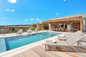Ein moderner Poolbereich im Freien mit Liegestühlen und einer überdachten Sitzgelegenheit.