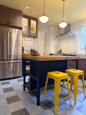 Eine moderne Küche mit einem Edelstahl-Kühlschrank, Holzschränken, einer schwarzen Arbeitsplatte und gelben Barhocker.