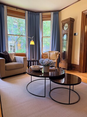 A living room with a sofa, a round table with a bowl and flowers, a chair, a lamp, and a clock. - Heart of Nova Scotia’s South Shore - Curated Luxury in a Landmark Home (Mahone Bay)