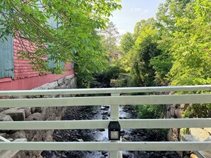 Eine Holzbrücke mit Geländer, darunter ein kleiner Bach und üppiges Grün.
