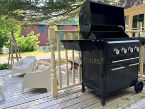 Ein schwarzer Grill für den Außenbereich mit vier Bedienelementen, ein weißer Stuhl und eine Holzterrasse.