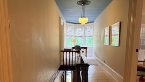 A hallway with a wooden staircase, a hanging light fixture, and a view of a dining area with chairs and a table. - Heart of Nova Scotia’s South Shore - Curated Luxury in a Landmark Home (Mahone Bay)