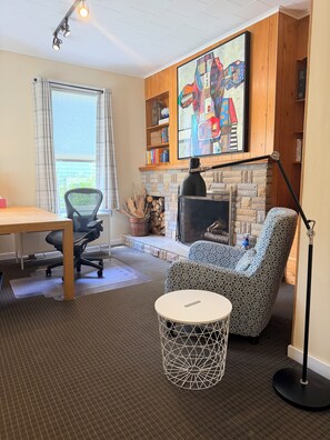 A cozy living room with a fireplace, a comfortable armchair, a dining table, and a bookshelf. - Heart of Nova Scotia’s South Shore - Curated Luxury in a Landmark Home (Mahone Bay)