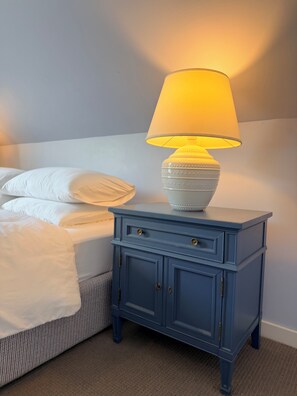 A bed with white linens, a blue nightstand with a lamp, and a wall with a light switch. - Heart of Nova Scotia’s South Shore - Curated Luxury in a Landmark Home (Mahone Bay)