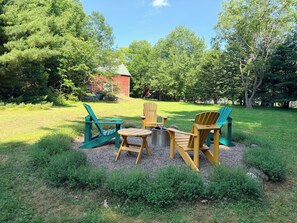 Ein Außenbereich mit Adirondack-Stühlen und einem Feuerkorb.