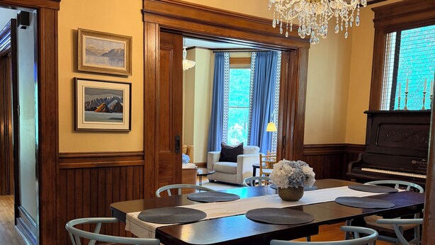 A dining area with a wooden table, blue chairs, a chandelier, and a piano. - Heart of Nova Scotia’s South Shore - Curated Luxury in a Landmark Home (Mahone Bay)