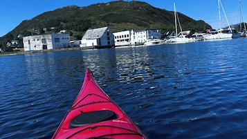 A red kayak on calm water with a view of a hill, buildings, and boats in the background.