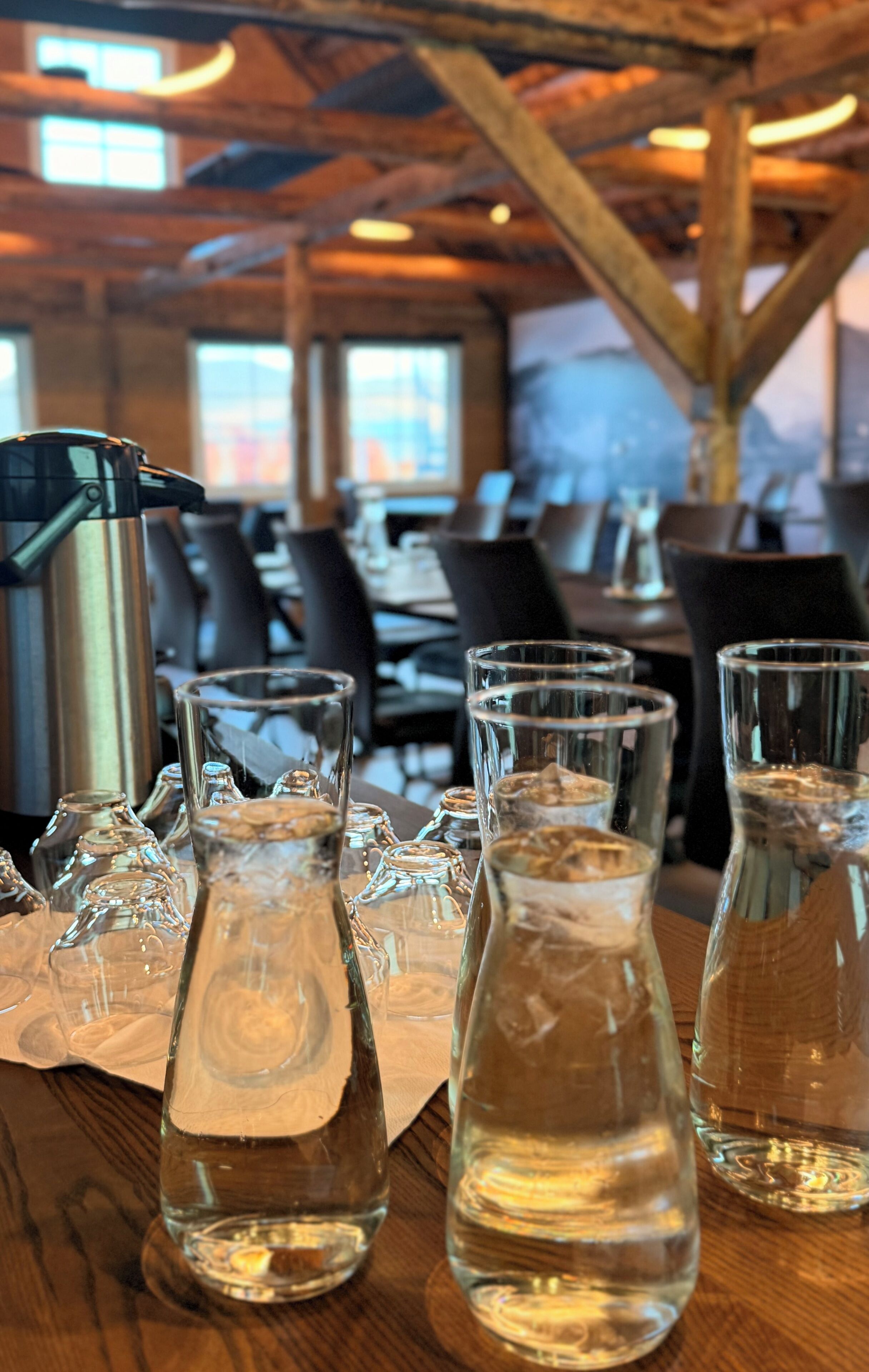 En bardisk med flera glas vatten och en kanna i rostfritt stål på ett träbord.