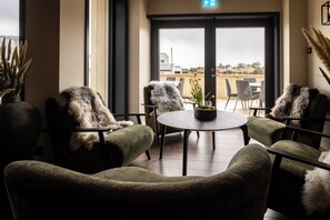A cozy seating area with plush chairs and a round table, overlooking a deck with outdoor seating. - Rosenlund Hamn (Sande)