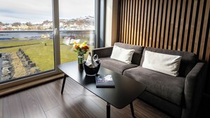 A modern living room with a grey sofa, a black coffee table, and a view of a body of water and buildings. - Rosenlund Hamn (Sande)